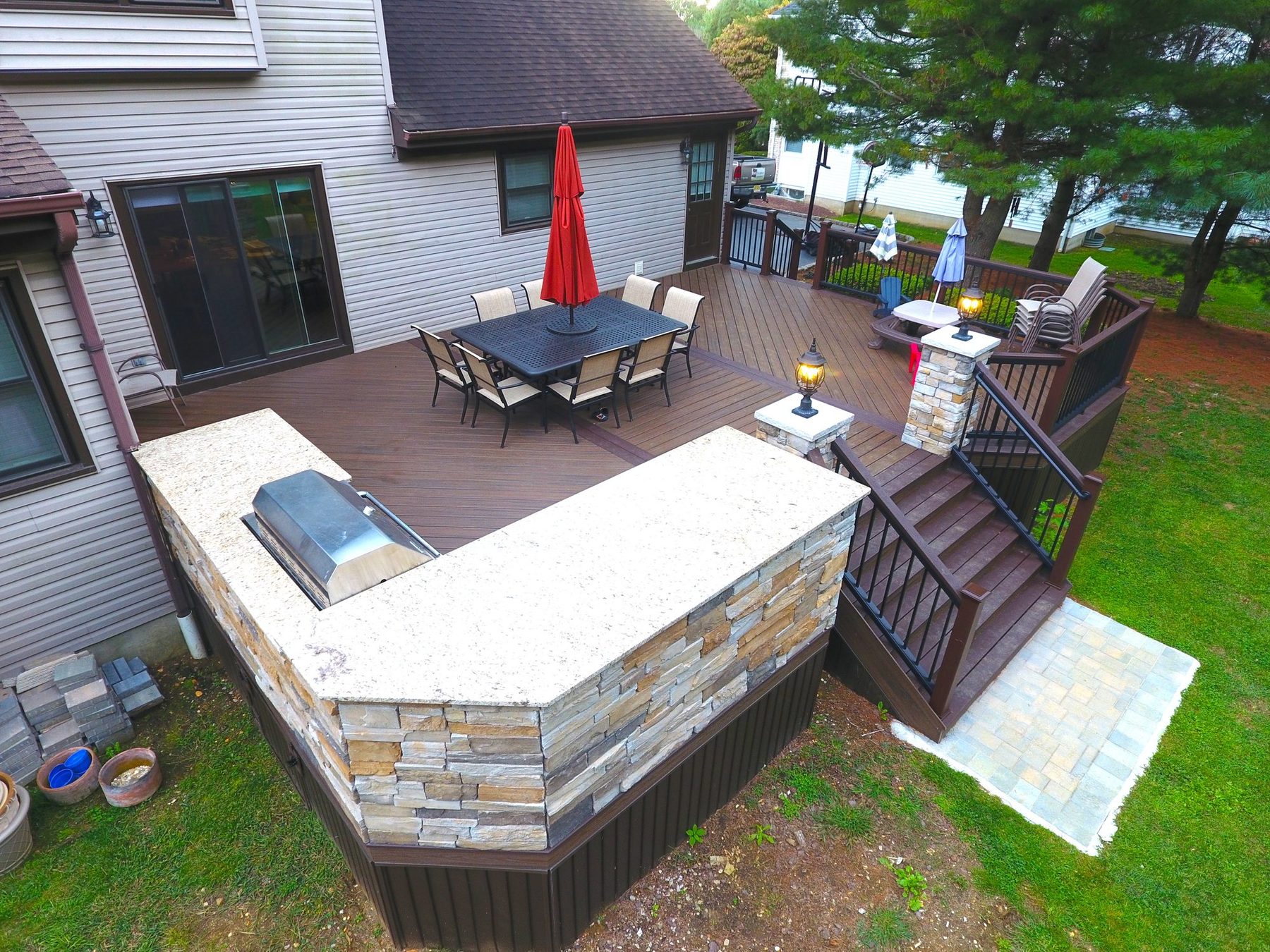 Multi-level composite deck with a stone built-in grill station, lit pillar caps and stairs to a paver landing